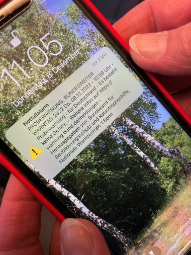 Zu sehen ist ein Smartphone mit einer Warnmeldung auf dem Startbildschirm. Die Warnmeldung kommt vom 'Cell Broadcast'-System.