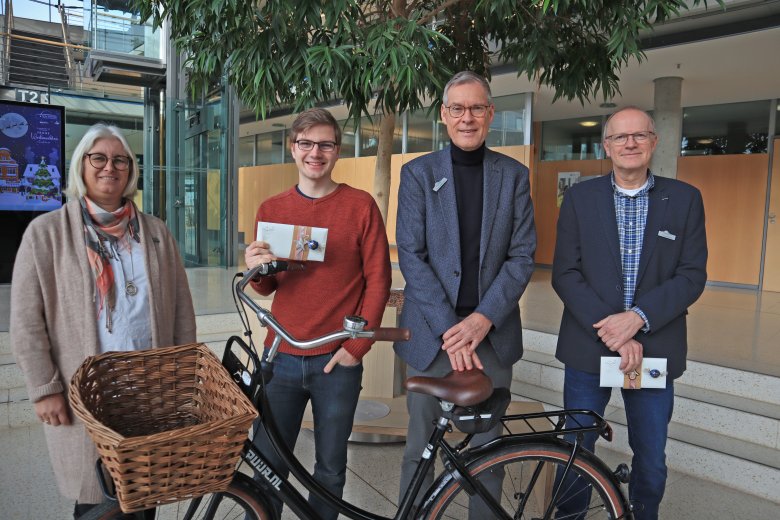 Vier Personen, zwei halten Gutscheine in den Händen, ein Fahrrad steht vor der Gruppe. 