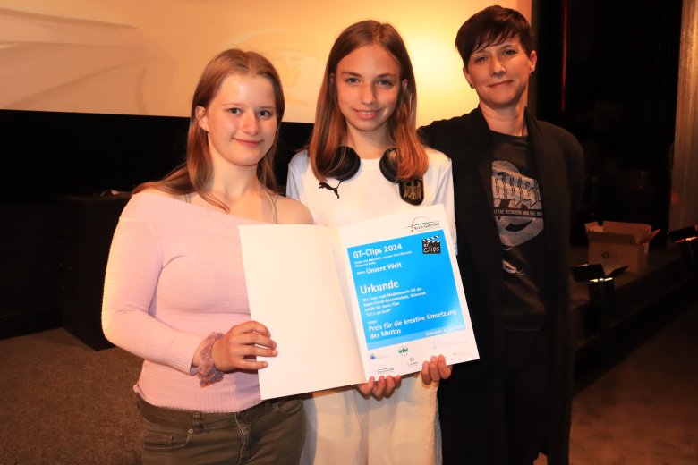 2 Mädchen mit Erwachsener, die Kinder halten eine Urkunde in der Hand. 