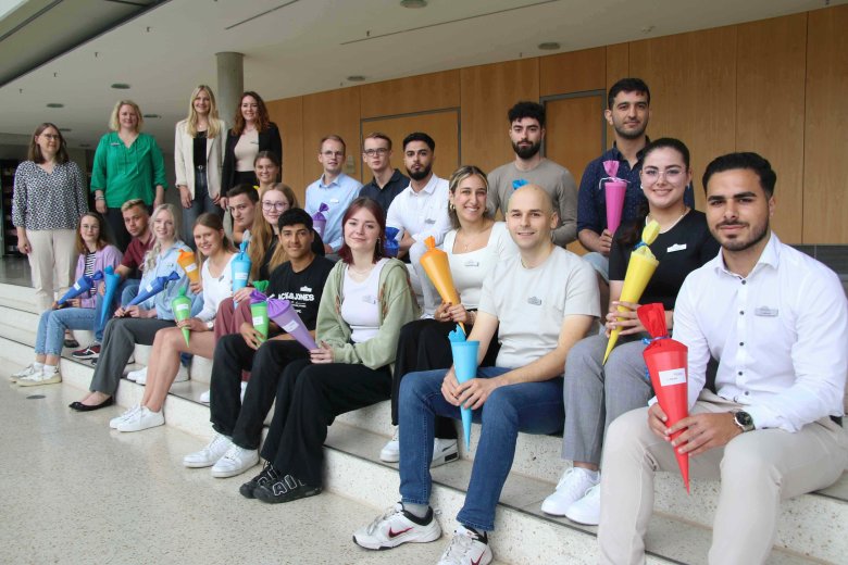 Vier Personen stehen im Foyer des Kreishauses Gütersloh, der Rest der Gruppe sitzt verteilt auf Stufen. Einige von ihnen halten Schultüten in der Hand.