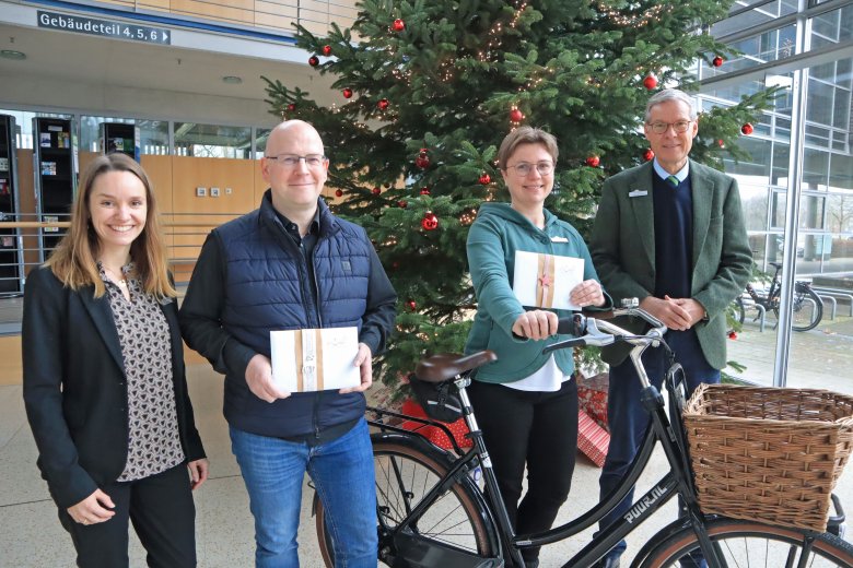 Personen stehen vor dem Weihnachtsbaum im Foyer des Kreishauses. Zwei Personen halten ein stehendes Fahrrad fest und haben Gutscheine in den Händen.