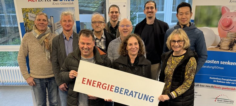 Personen stehen nebeneinander und blicken in die Kamera. Sie halten ein Banner mit der Aufschrift 'Energieberatung' in den Händen. 