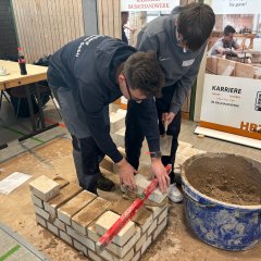 Ein Mann zeigt einem Schüler, wie man eine Mauer baut.